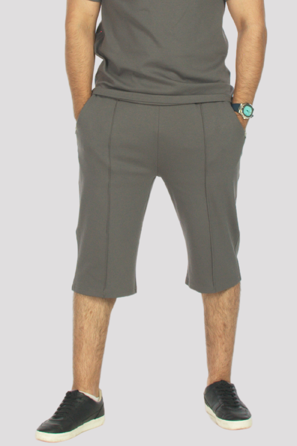Person wearing grey 3/4 shorts and a grey polo shirt on a plain background