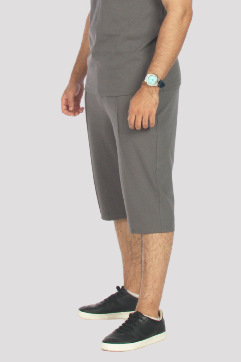Person wearing grey 3/4 shorts and grey polo shirt light grey background