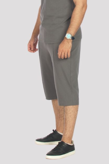 Person wearing grey 3/4 shorts and grey polo shirt light grey background